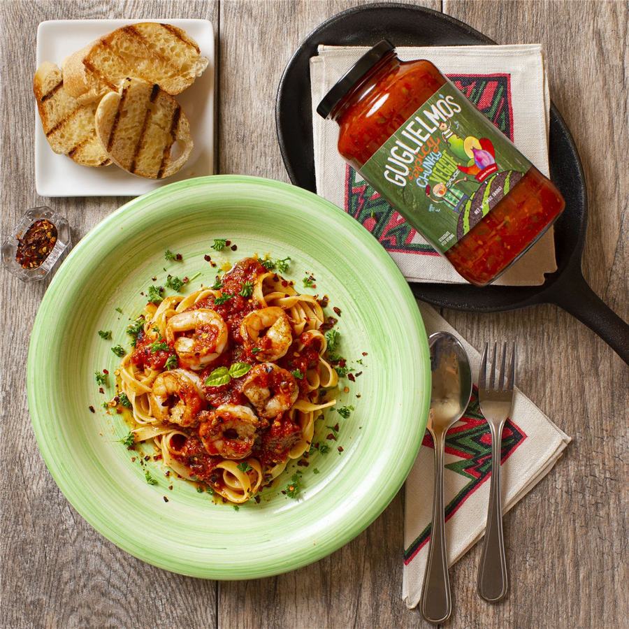 Shrimp over fettuccine in a red sauce on a green plate, with a jar of Spicy Chunky Veggie sauce and grilled bread