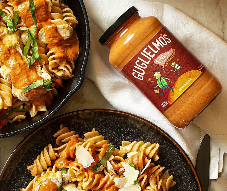 Sliced chicken and spiral pasta in a creamy Rosa sauce with basil ribbons and parmesan, next to a jar of Rosa