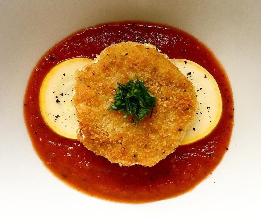 A golden breaded goat cheese fritter on yellow squash in a pool of marinara sauce