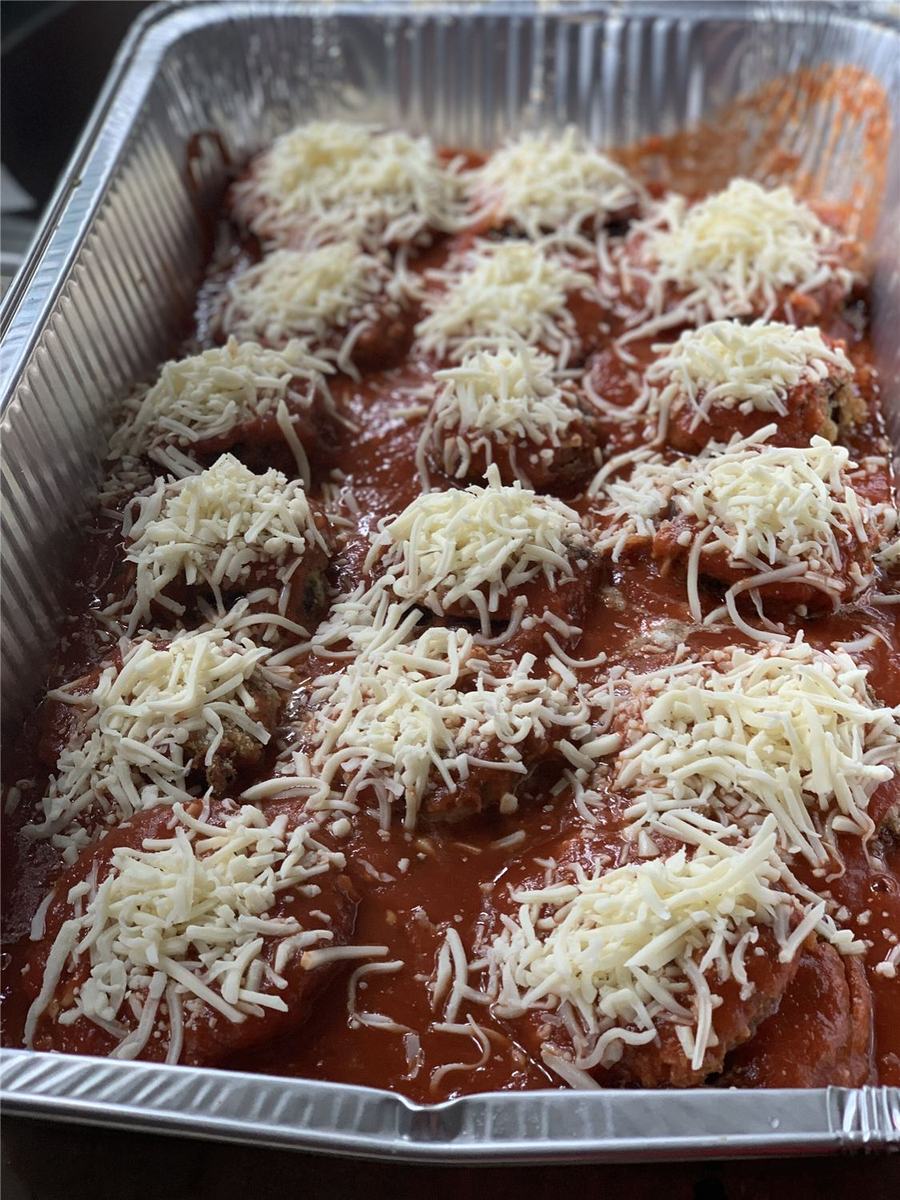 A foil pan of breaded eggplant parm topped with tomato sauce and shredded mozzarella