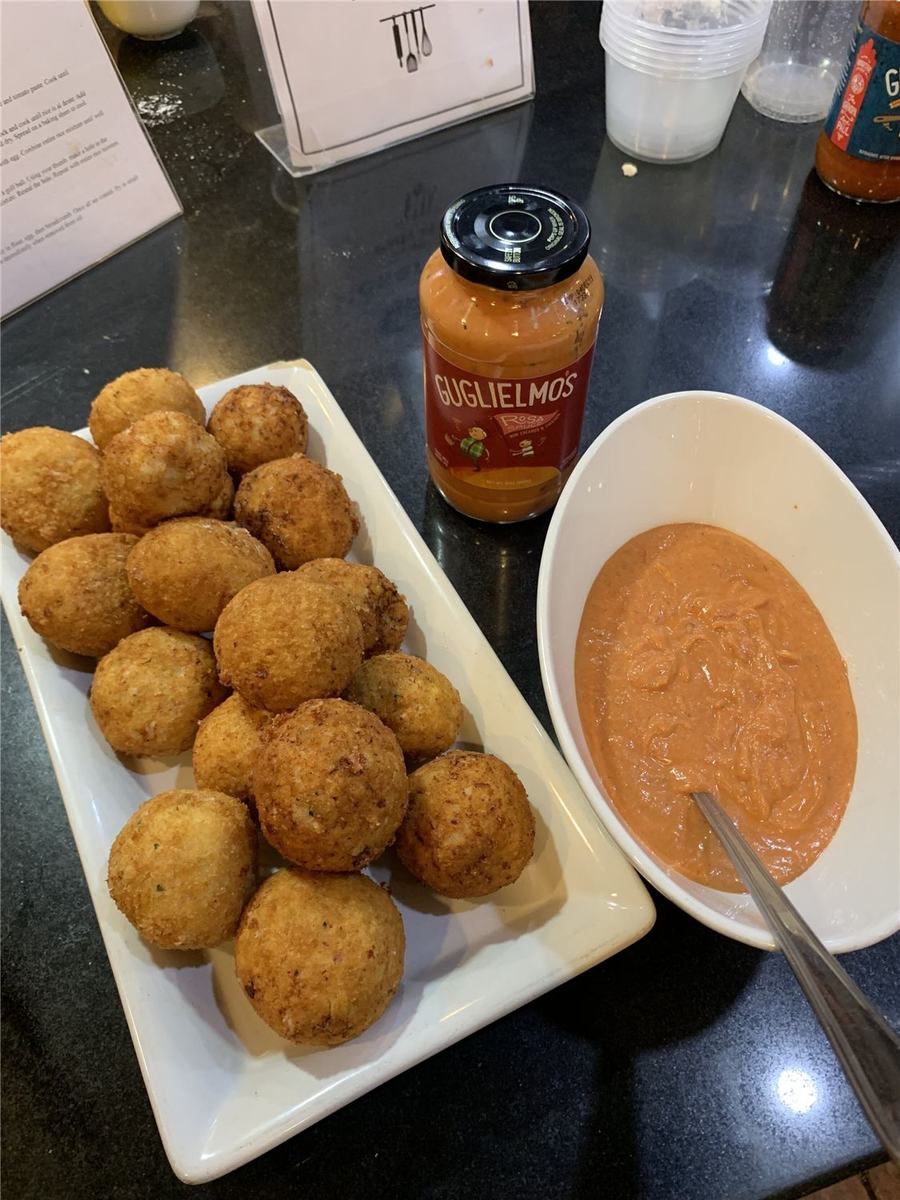 Golden fried arancini rice balls on a white plate beside a jar of Guglielmo's Rosa sauce and a bowl of the sauce for dipping