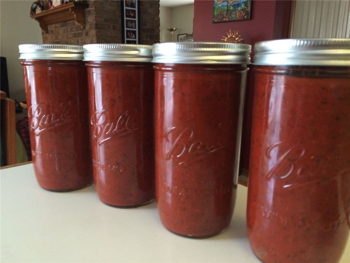 Four jars of red tomato sauce with silver lids lined up on a white counter