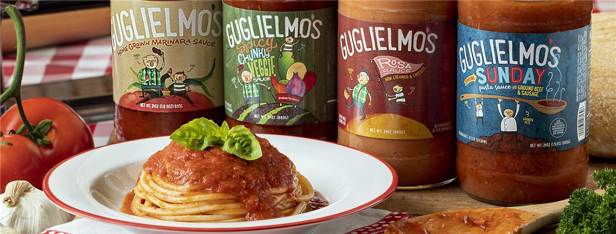 Four Guglielmo's jars lined up behind a plate of spaghetti topped with basil